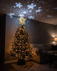 Stella gold glitter star tree topper lit on a Christmas tree, snowflakes projected across the ceiling