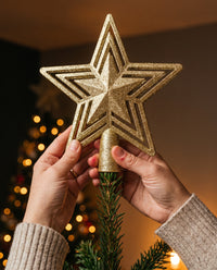 Hands placing the Stella star topper on the tip of a Christmas tree