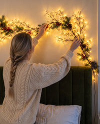 A woman bending a section of the lit branch into a curve against the wall by hand