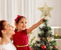 A child placing the Stella gold star on top of the family Christmas tree