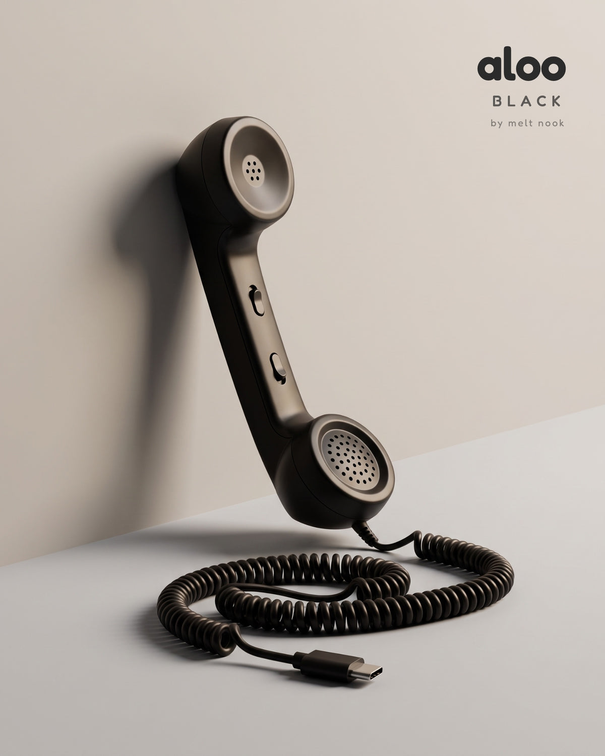 Aloo in black standing against a light grey wall, its coiled USB-C cord on the floor