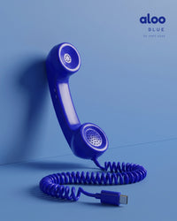 Aloo in blue standing against a blue wall, its coiled USB-C cord on the floor