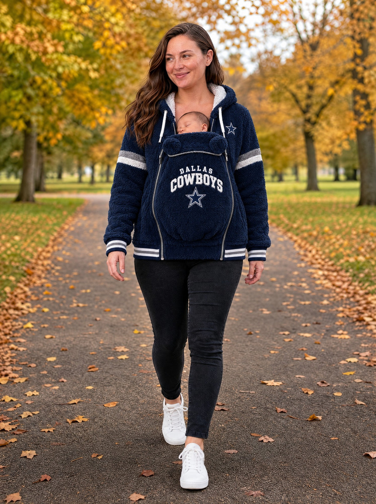 Mom walking in an autumn park wearing the Game Day Carrier Hoodie with her baby