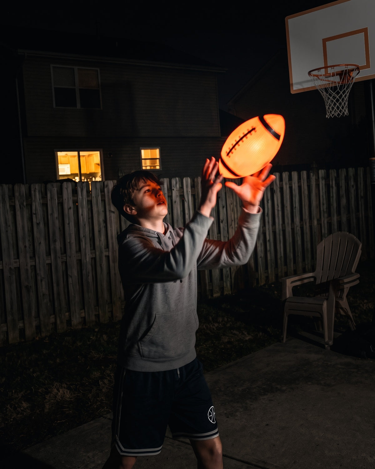 Teen catching a glowing Glow Ball football in a dark backyard at night