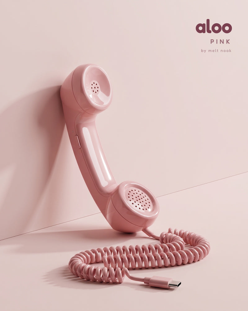Aloo in pink standing against a blush wall, its coiled USB-C cord on the floor