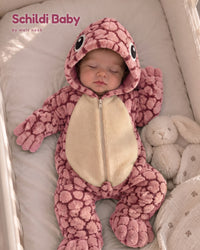 Baby schläft im Babybett im rosa Schildi Baby Overall neben einem Plüschhasen