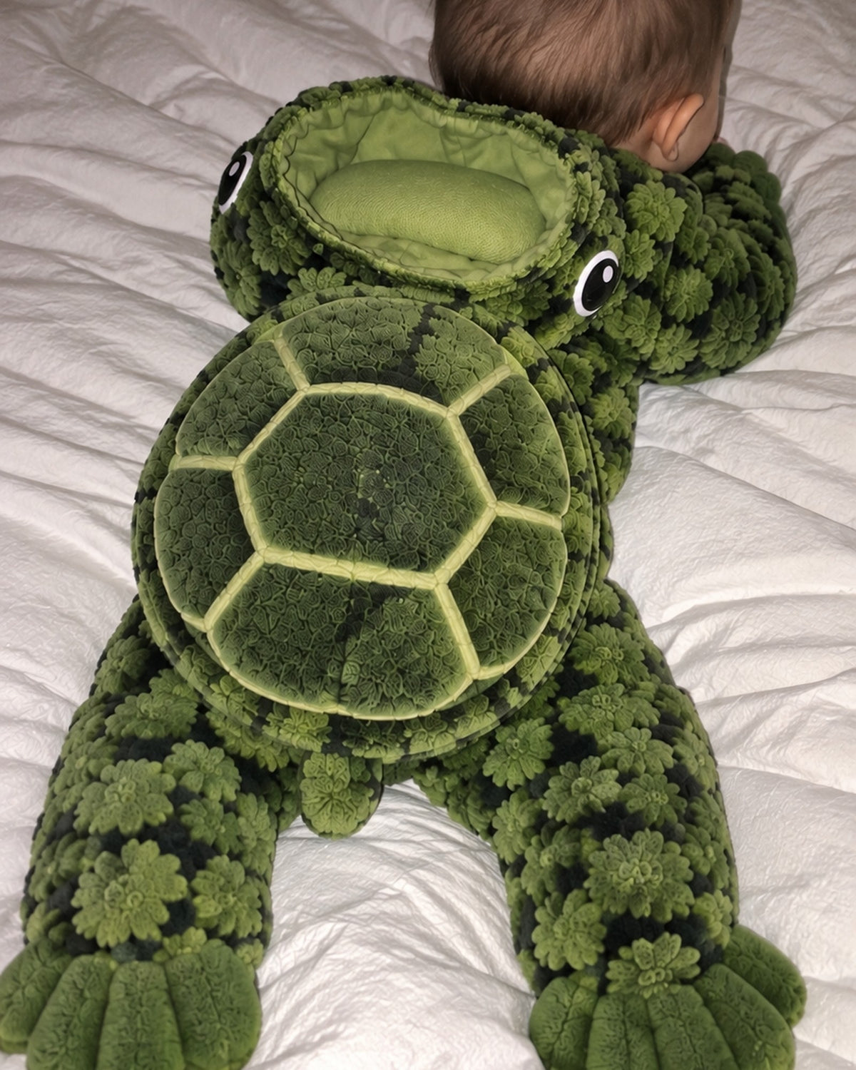 Baby lying on their tummy showing the padded shell of the Turtle Baby onesie