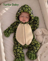 Baby asleep in a crib in the green Turtle Baby onesie next to a plush bunny