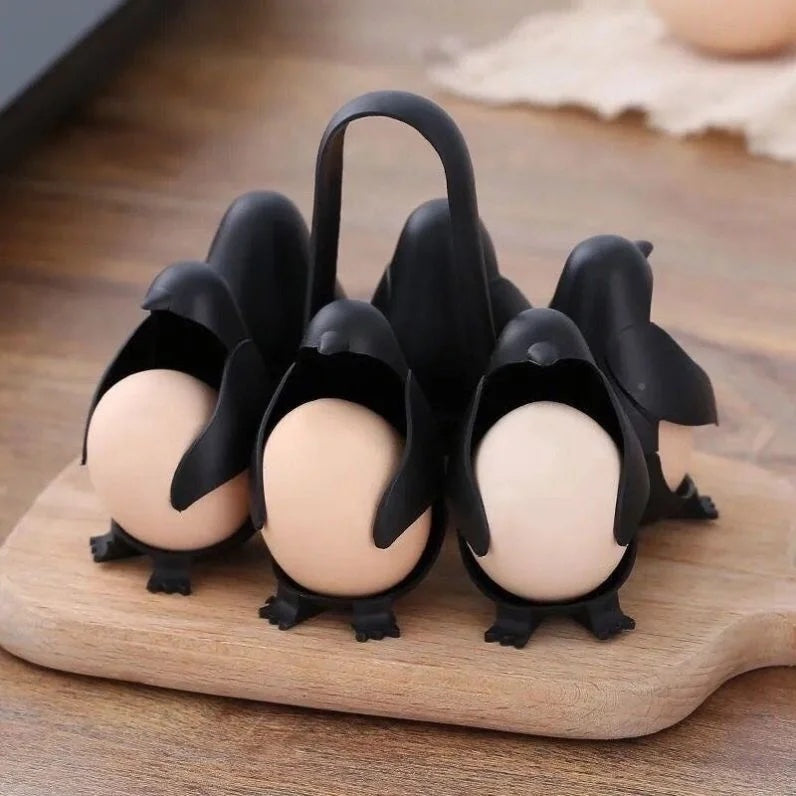 Six black penguin egg holders, each cradling a boiled egg, standing on a wooden board