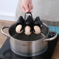 The penguin egg holder being lowered by its handle into a pot of boiling water