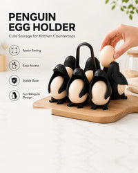 Six penguin egg holders on a wooden board, a hand placing an egg into one. Labelled: penguin egg holder, cute storage for kitchen countertops, space saving, easy access, stable base, fun penguin design.